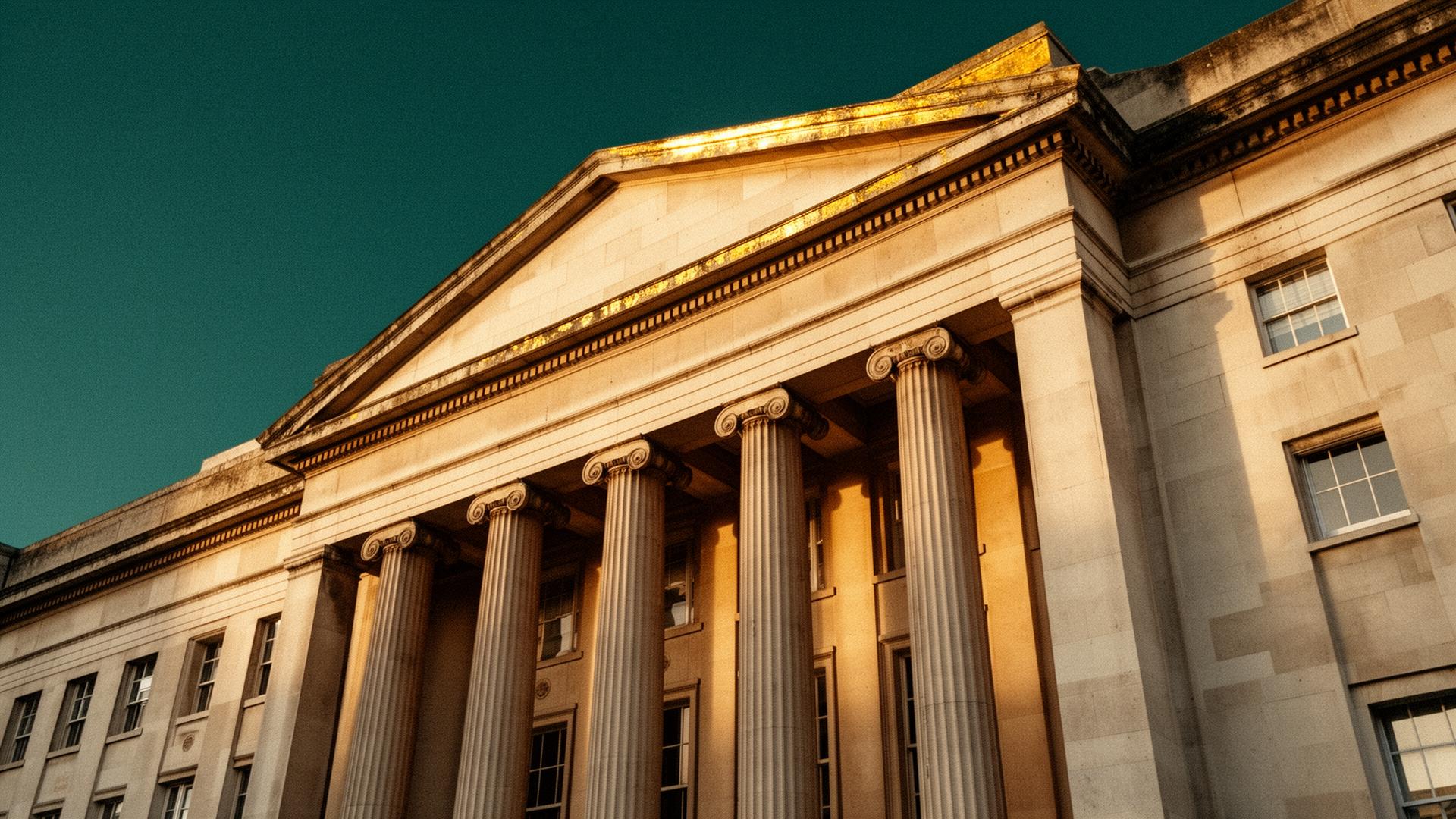 Neoclassical stone columns of a British courthouse facade lit by morning light